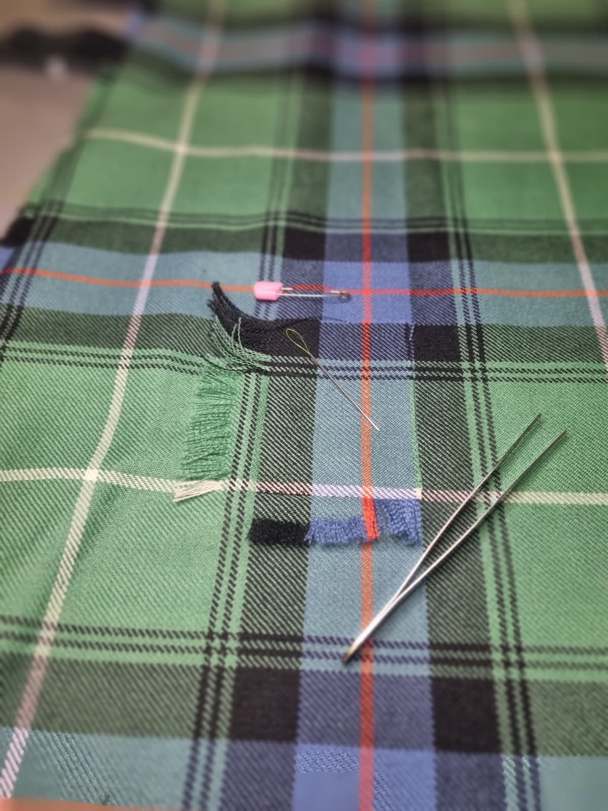 Green and blue tartan fabric with a small puncture hole and frayed fibres.