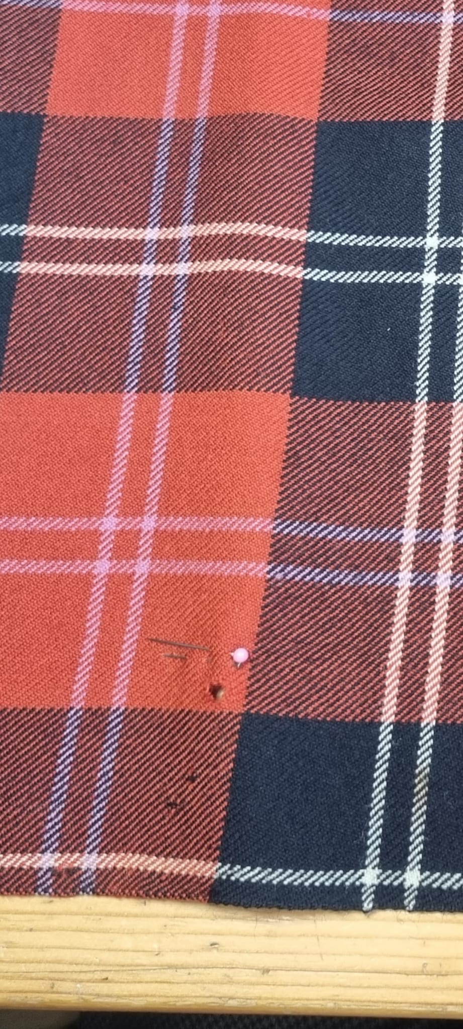 Orange and navy tartan kilt with small moth hole marked by a pin.